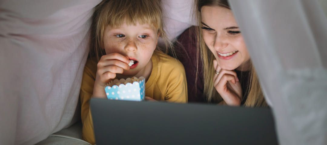 Photo of a woman and a child looking at a computer under pillows