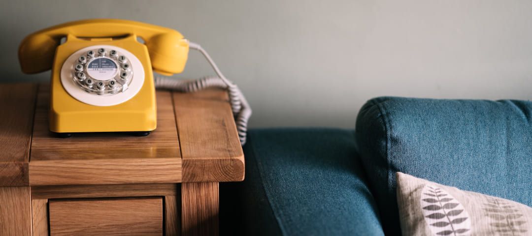 Photo of an old-fashioned yellow telephone on a table beside a couch