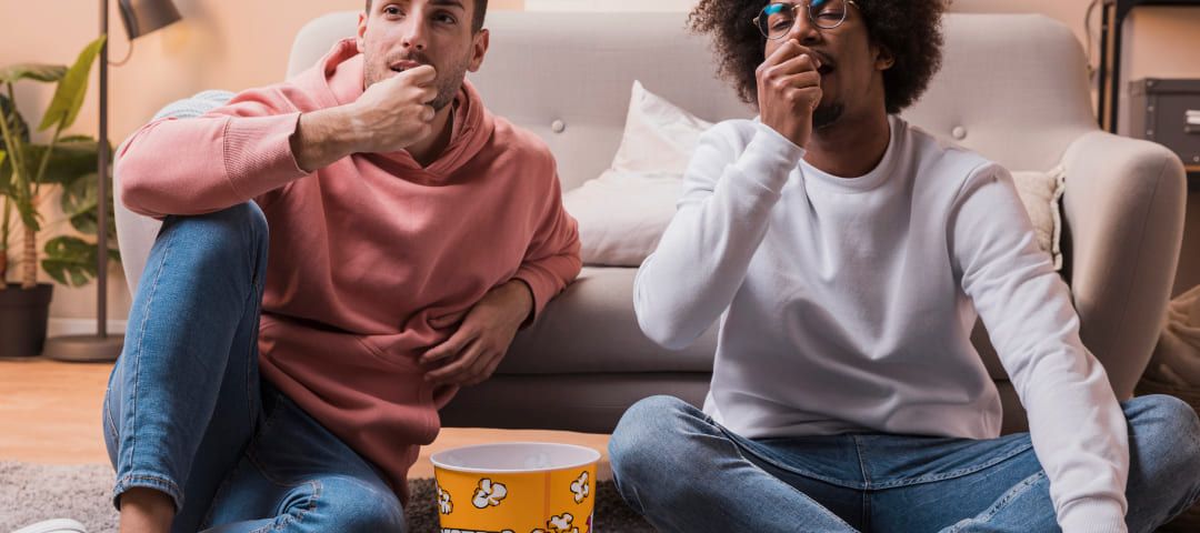 Photo of two men sitting in front of a couch eating popcorn