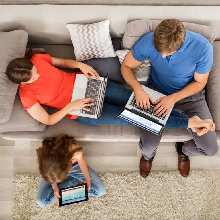 WTC Communications Kingston - Overhead view of a family using laptops and a tablet on a sofa.